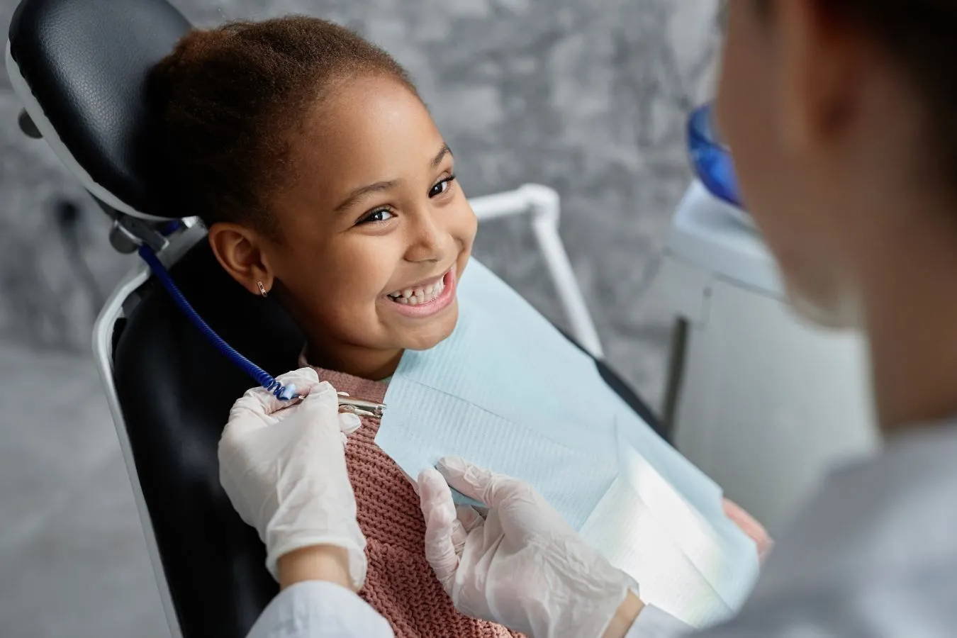 Young child smiling at orthodontist as they place a napkin around her neck