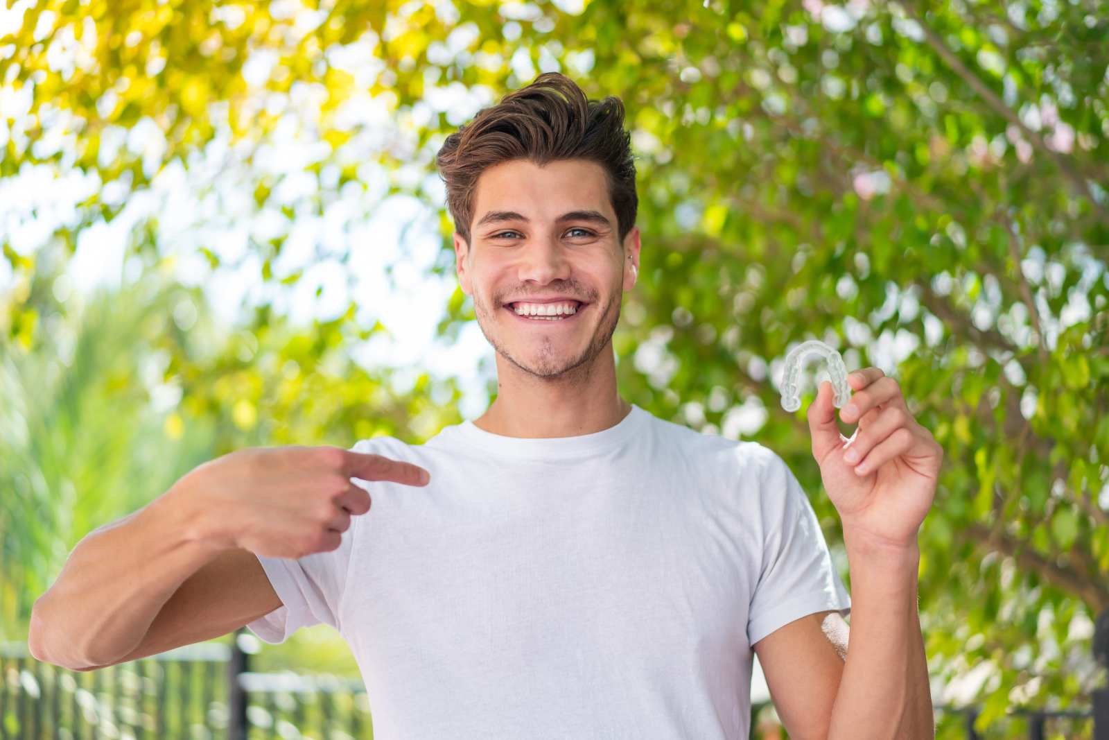 A man holding up a clear aligner and pointing at it